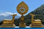 Ornate Buddhist prayer wheel with golden deer statues and mountain backdrop.
