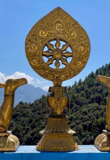 Ornate Buddhist prayer wheel with golden deer statues and mountain backdrop.